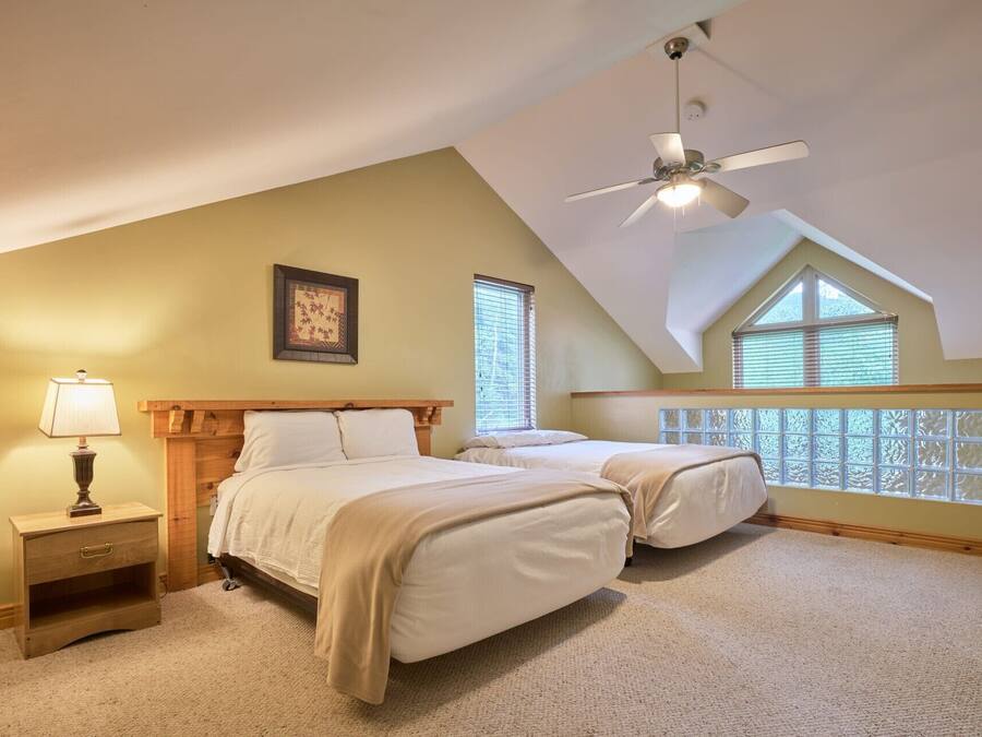 A bedroom with two beds, a ceiling fan, a nightstand, and a window with blinds.