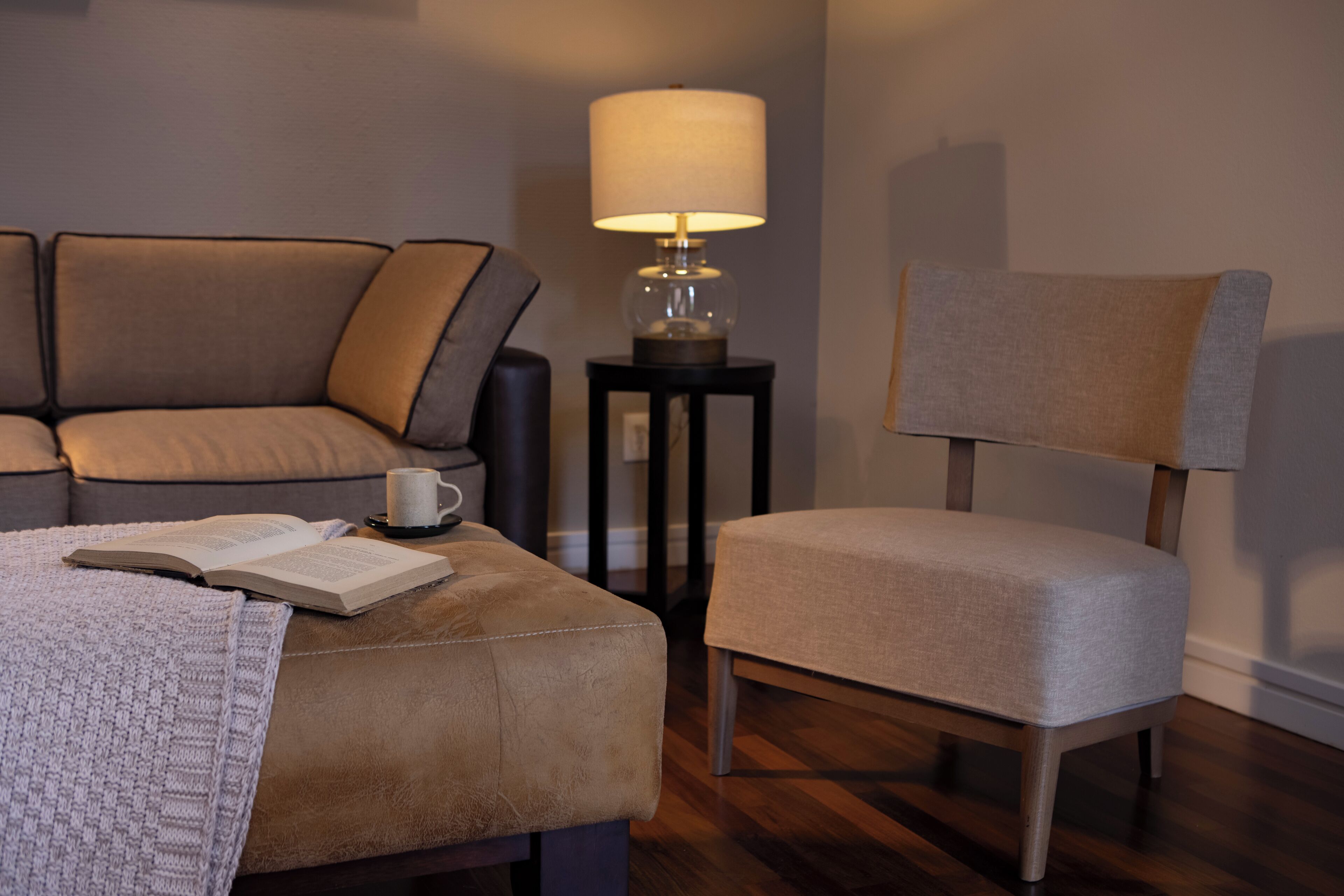 A cozy living room with a sofa, ottoman, and chair, a lamp, and a book on the ottoman.