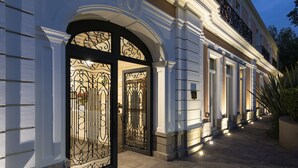 Een statig toegangspunt met versierde ijzeren poorten en een verlicht pad dat naar een gebouw met klassieke architectuur leidt.