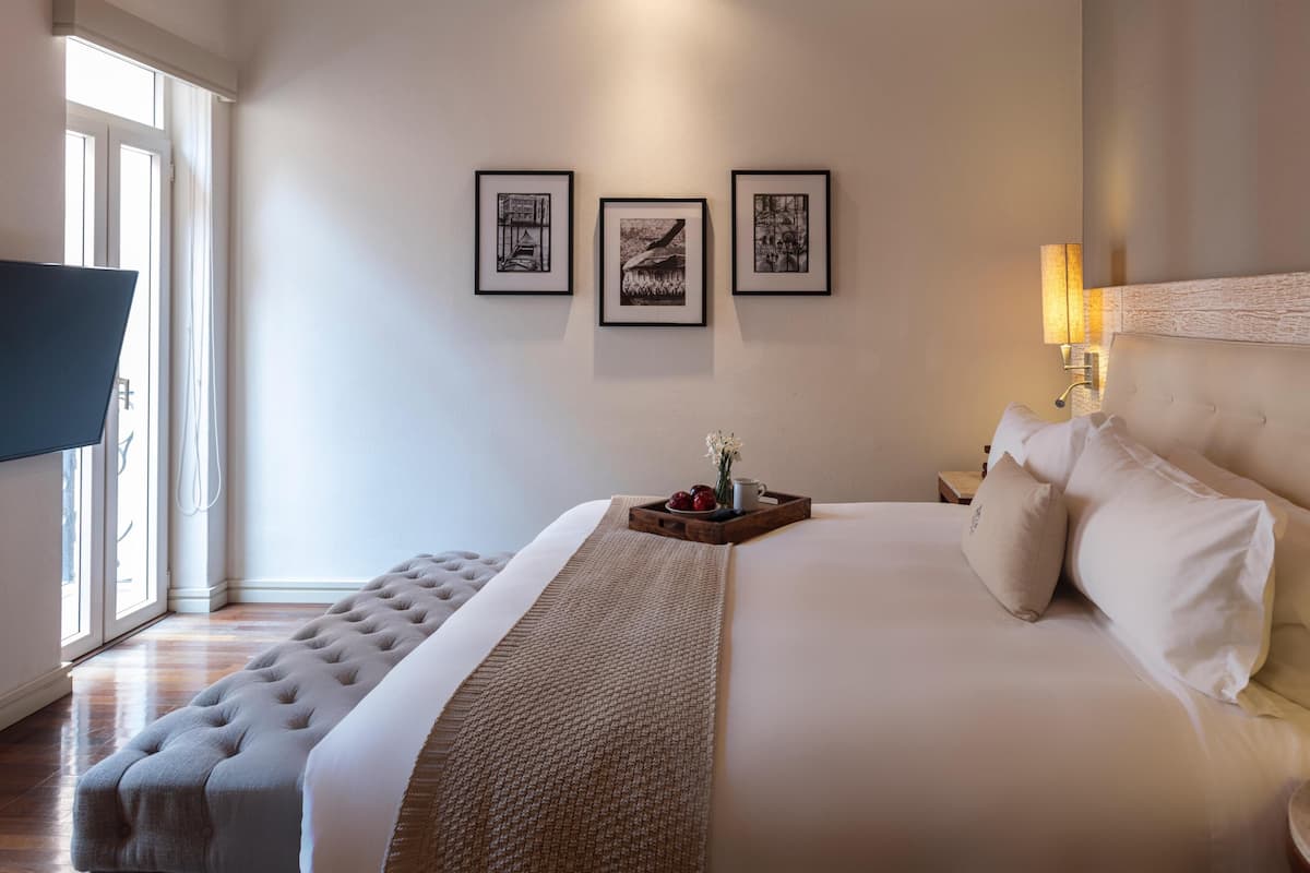Une chambre d’hôtel avec un grand lit, une télévision, une fenêtre avec des rideaux et trois tableaux encadrés accrochés au mur.