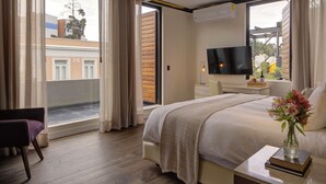 Een hotelkamer met een groot bed, een nachtkastje met een boek en een bloevas, een aan de muur bevestigde televisie en een raam met gordijnen.