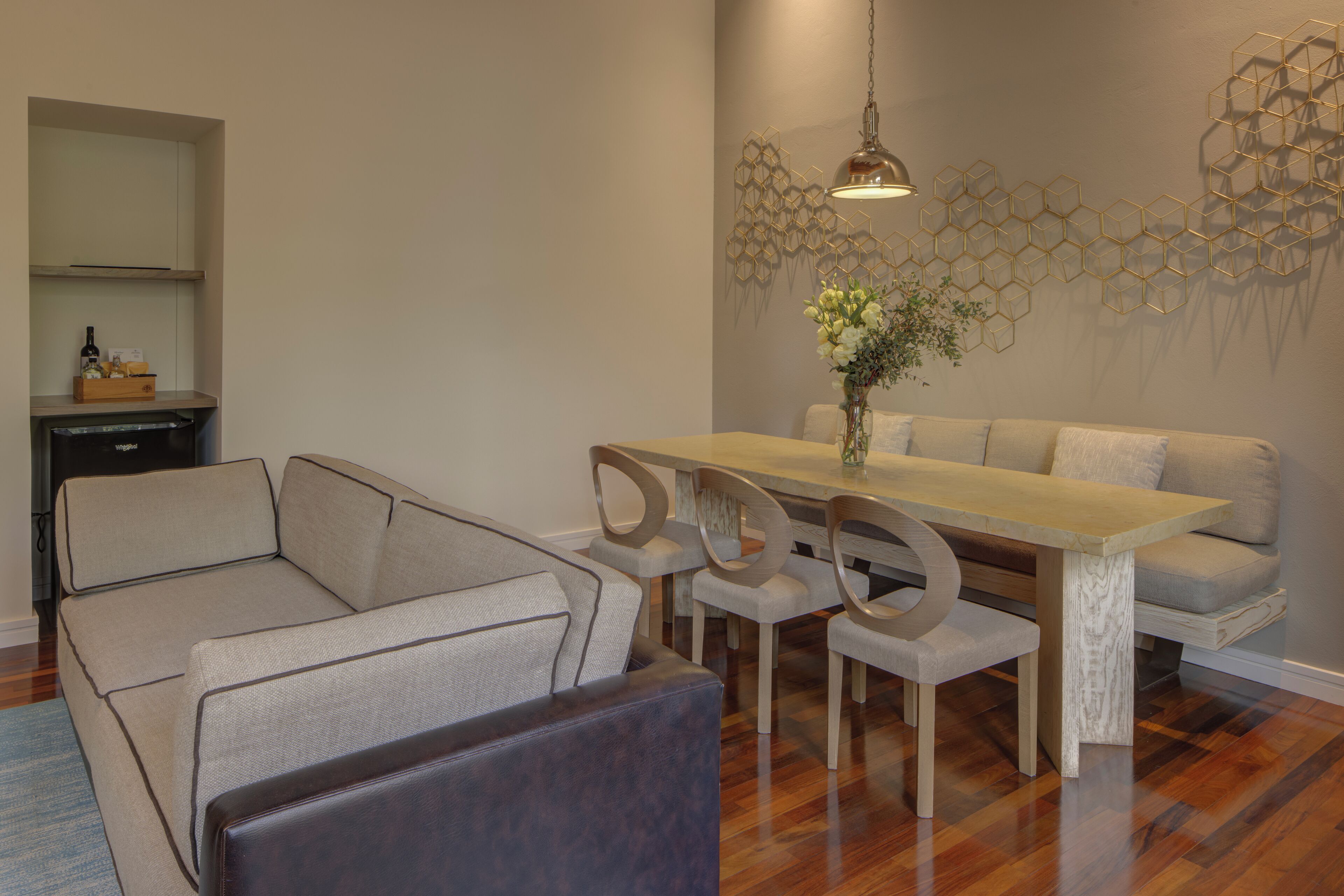 A modern living room with a wooden dining table, grey sofas, and a decorative wall piece.
