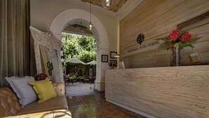 Een receptiegedeelte met een houten receptiebalie, een bank met kussens en een boogvormige doorgang naar een terras.