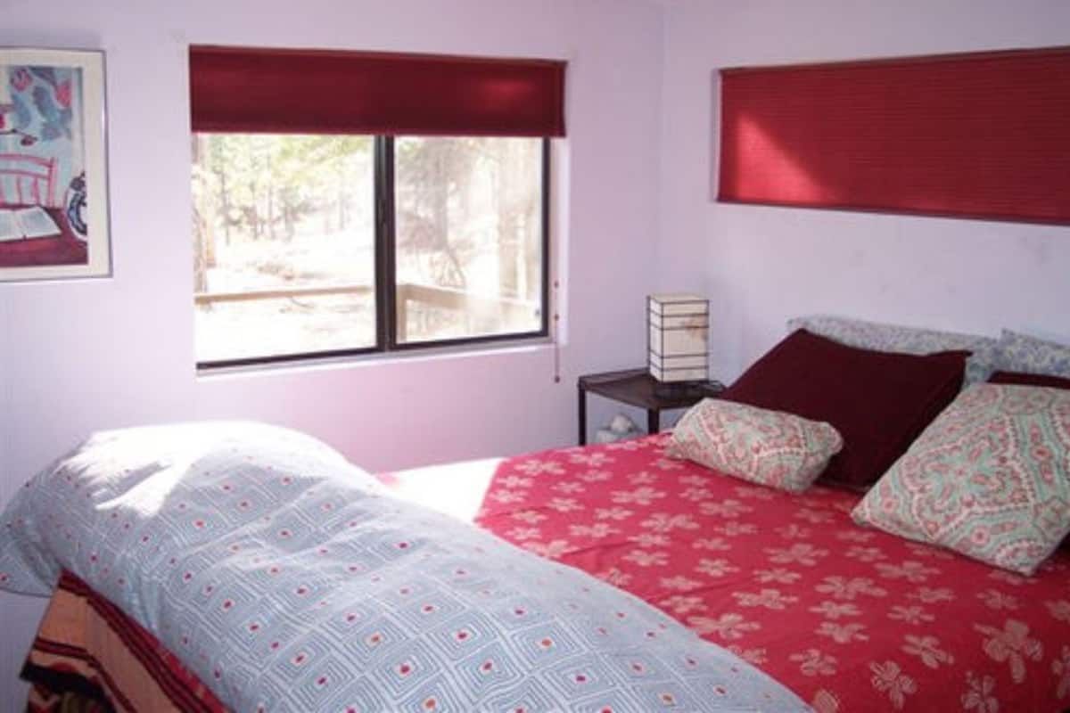 A bedroom with a bed, a window with a view, a bedside table, and a painting on the wall.
