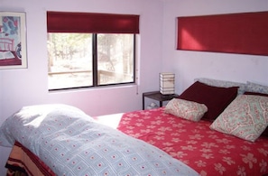 A bedroom with a bed, a window with a view, a bedside table, and a painting on the wall.