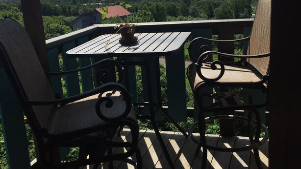 A wooden deck with two chairs and a table, overlooking a mountainous landscape and a body of water. - Homer Stay and Play (Homer)