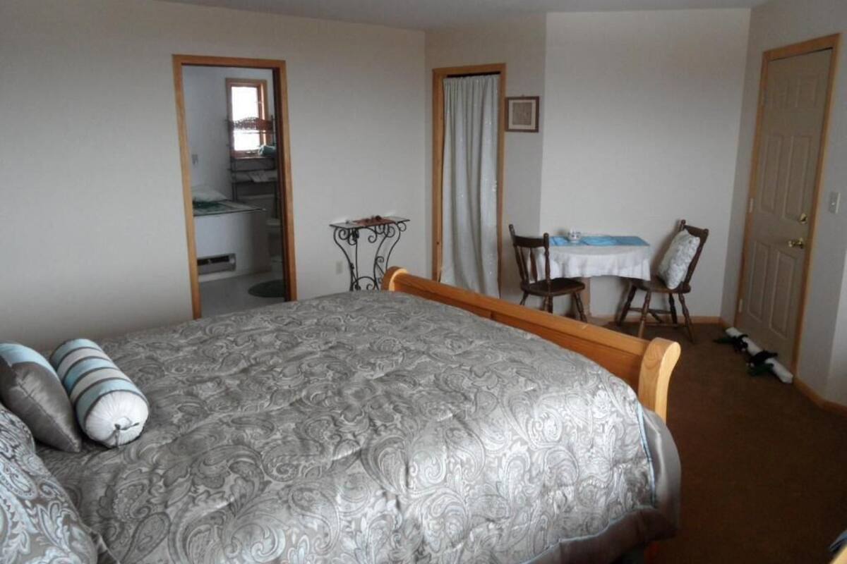A bedroom with a bed, a chair, a table, and a door.