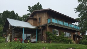 A rustic wooden house with a porch and a balcony. - Homer Stay and Play (Homer)