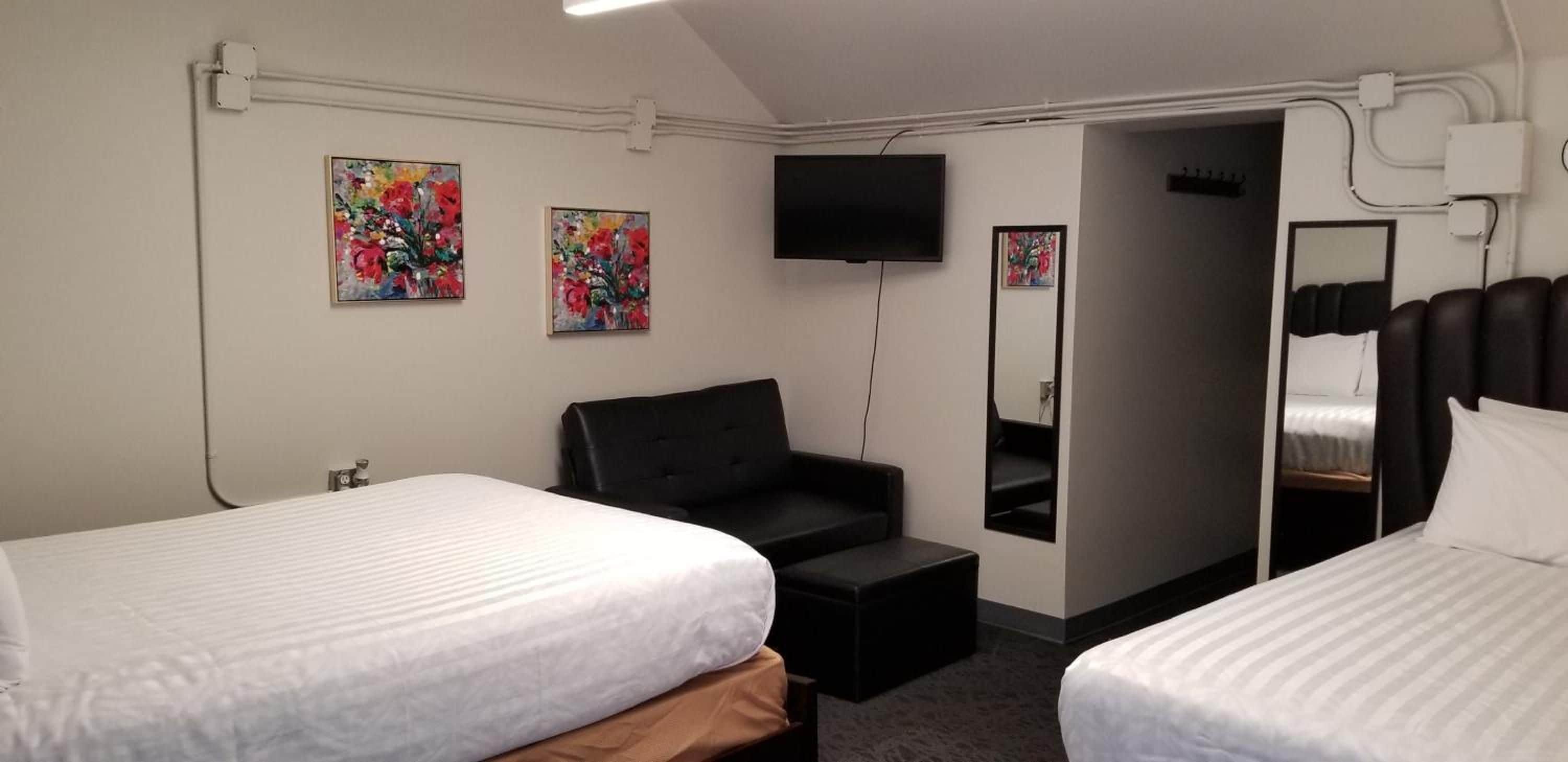 Habitación de hotel con dos camas, un sofá, un televisor y obras de arte en las paredes.