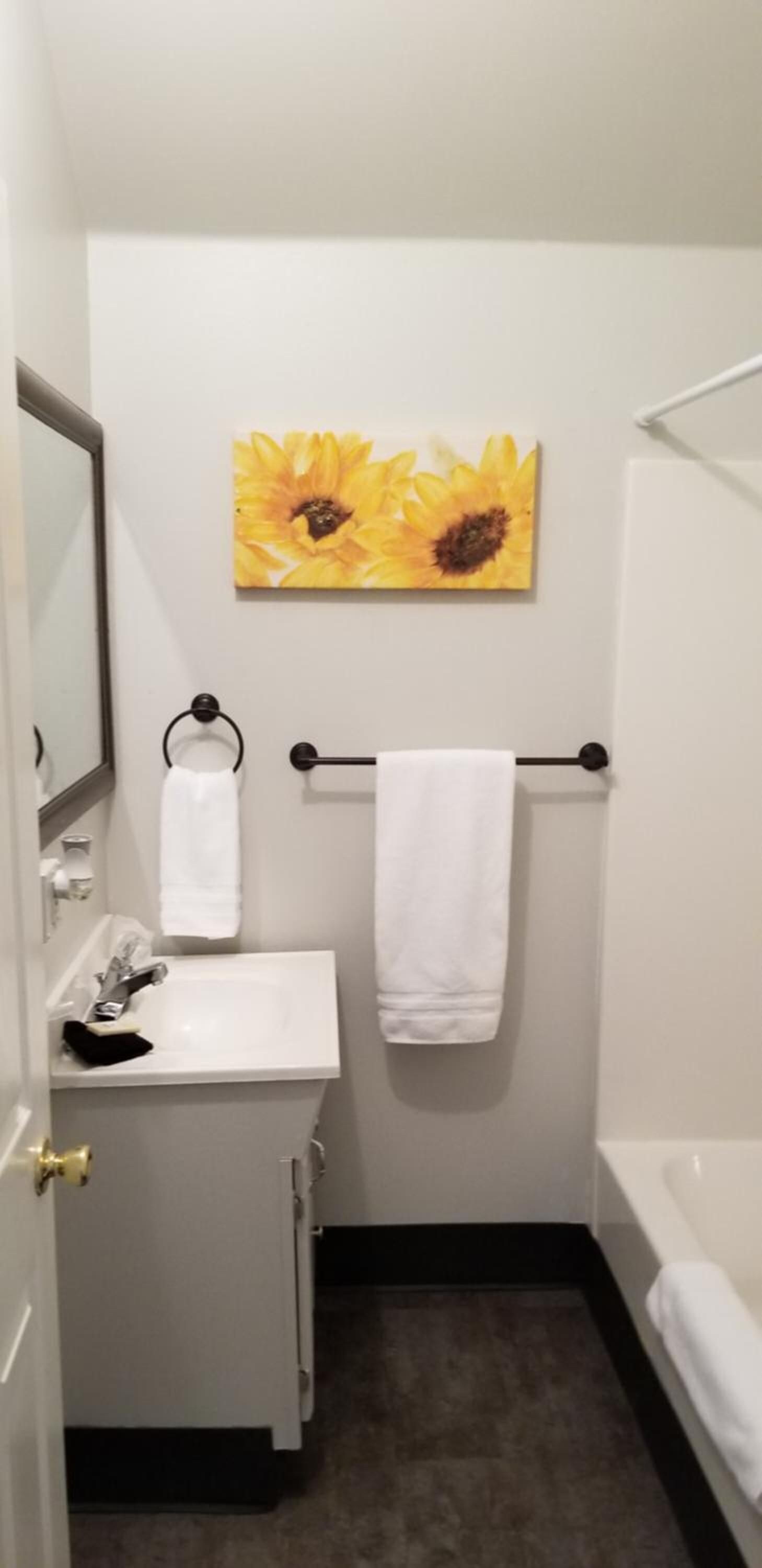 Un baño con lavamanos, espejo, toallero y un cuadro de girasoles en la pared.