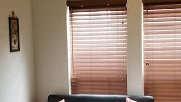 A black leather sofa with two patterned pillows, a framed picture on the wall, and a sign that reads 'VINEYARD' above two windows with blinds.