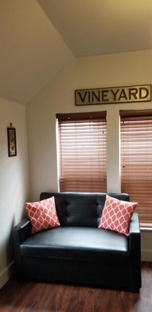 A black leather sofa with two patterned pillows, a framed picture on the wall, and a sign that reads 'VINEYARD' above two windows with blinds. - Deep Water Inn (Chelan)