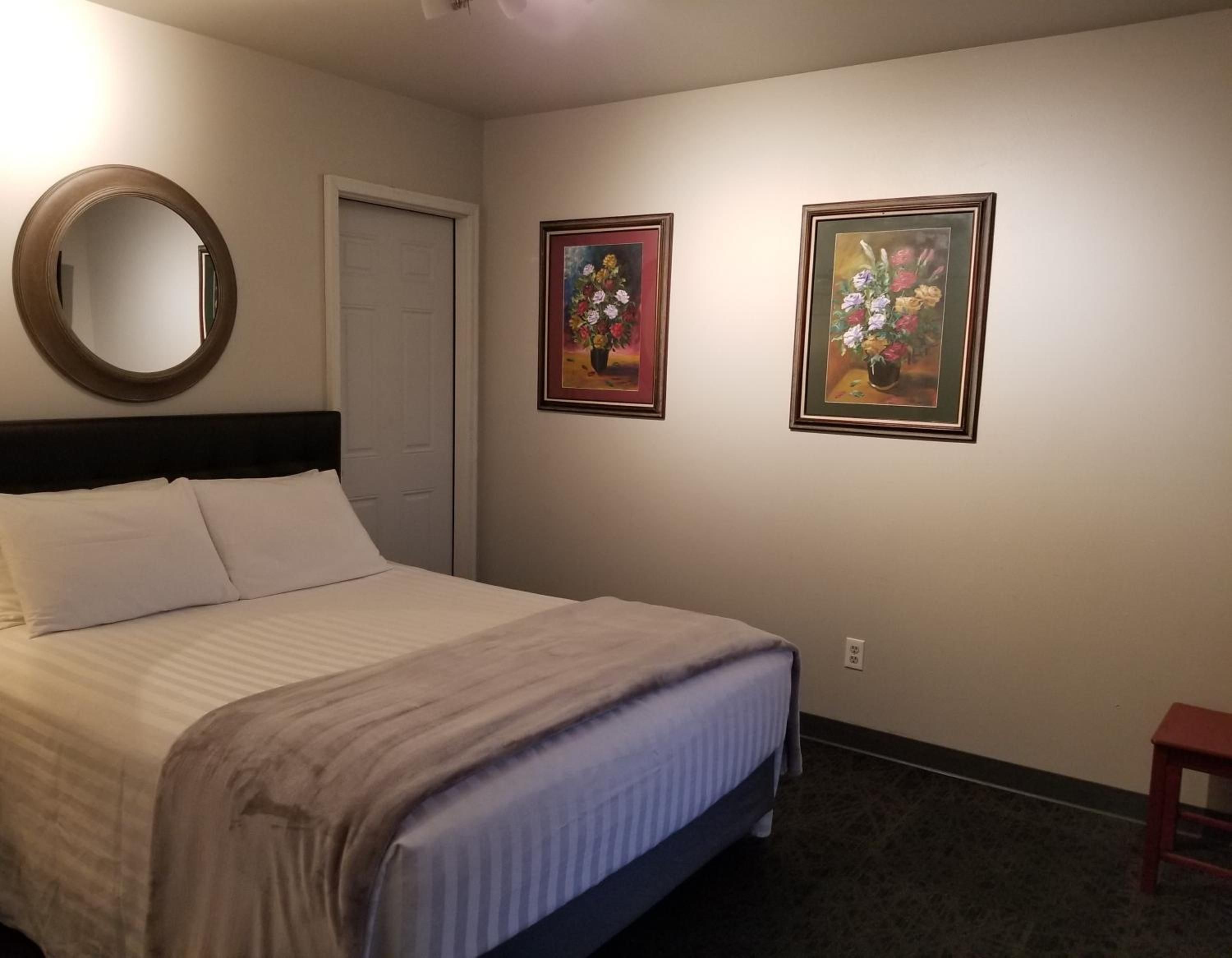 A hotel room with a bed, a round mirror, and two framed floral paintings on the wall.