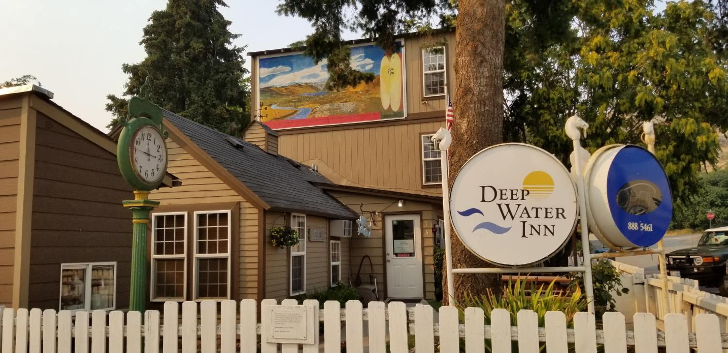 Un bâtiment orné d’une horloge, d’une enseigne indiquant un hôtel appelé « Deep Water Inn », et d’une fresque sur le mur latéral.