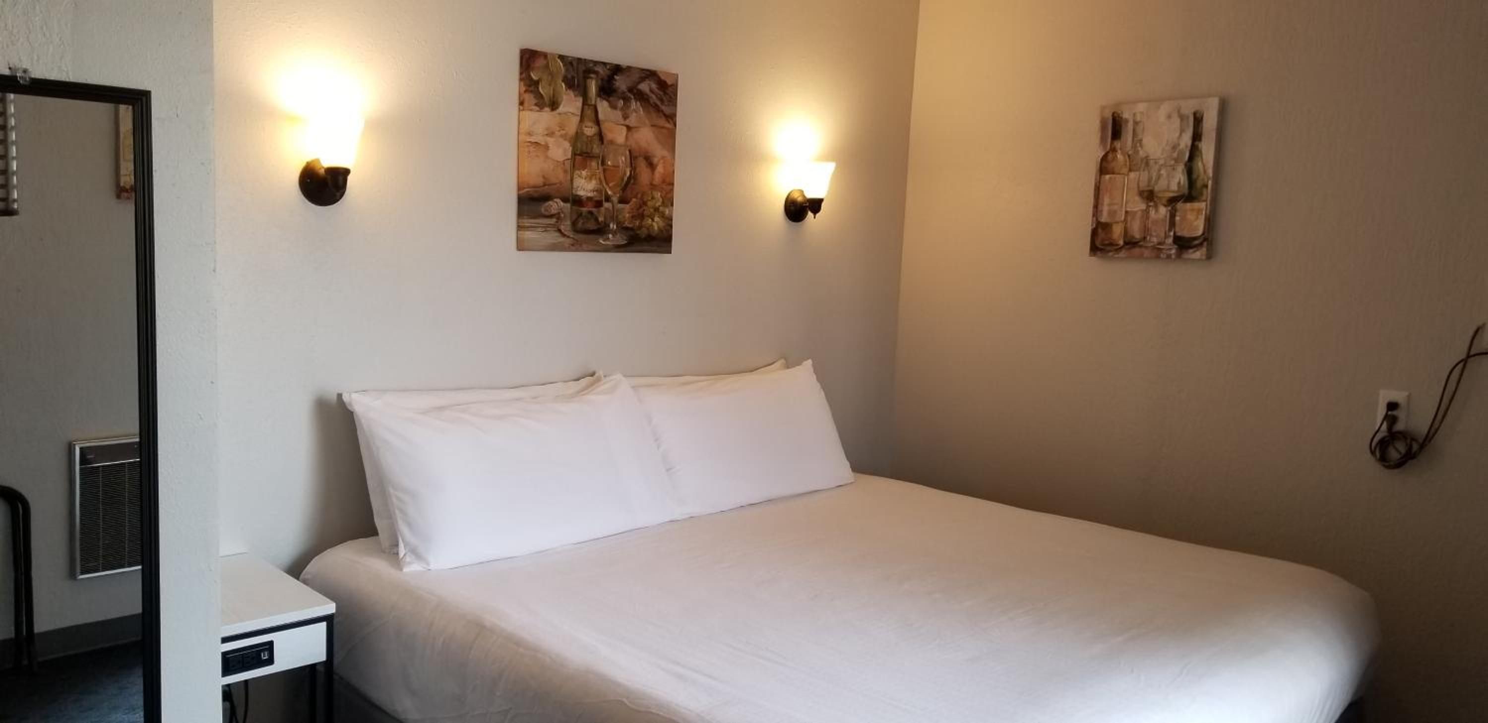 A single bed with white bedding in a room with two wall-mounted light fixtures and two paintings.