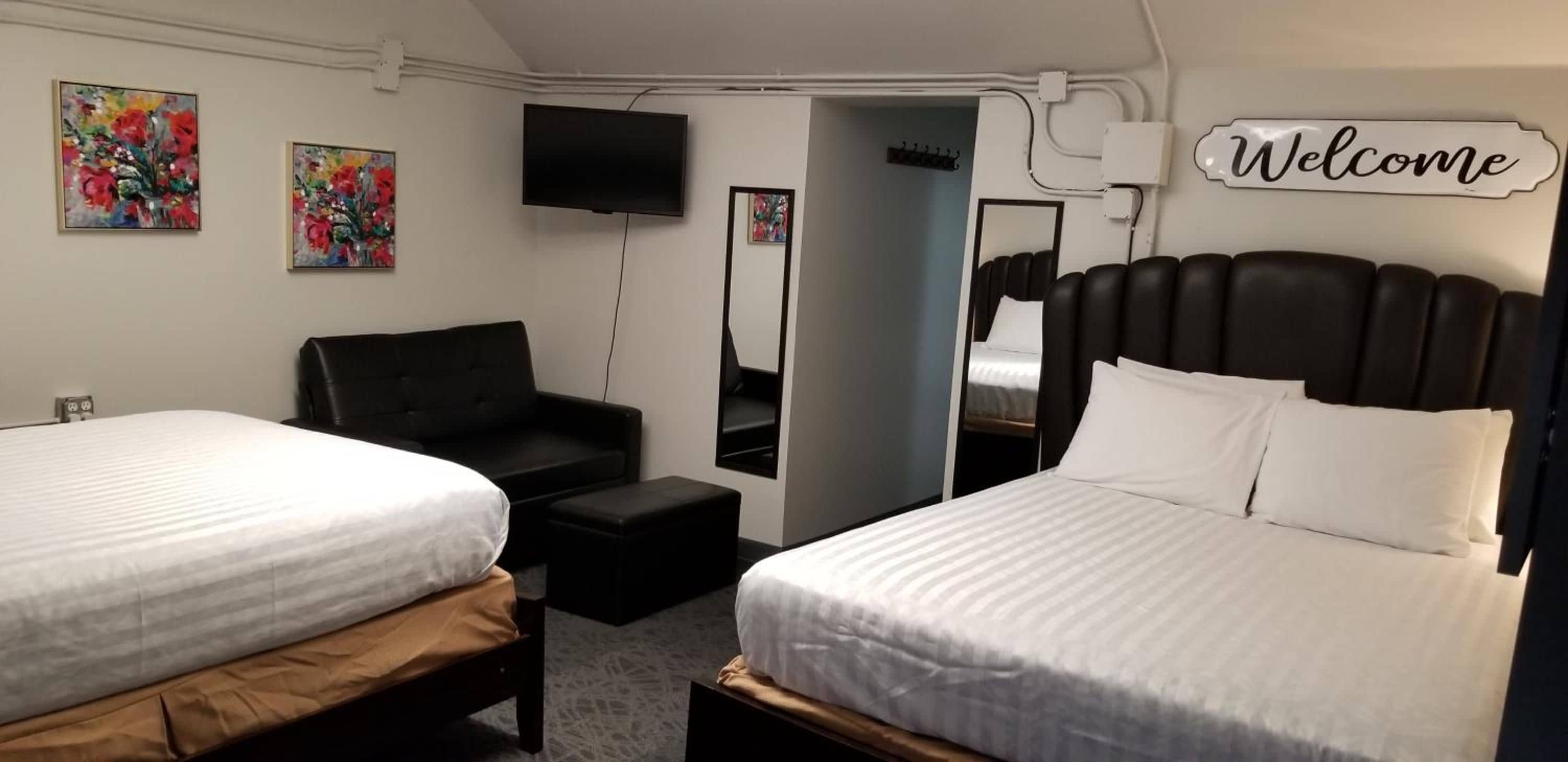 A hotel room with two beds, a sofa, a TV, and a 'Welcome' sign.