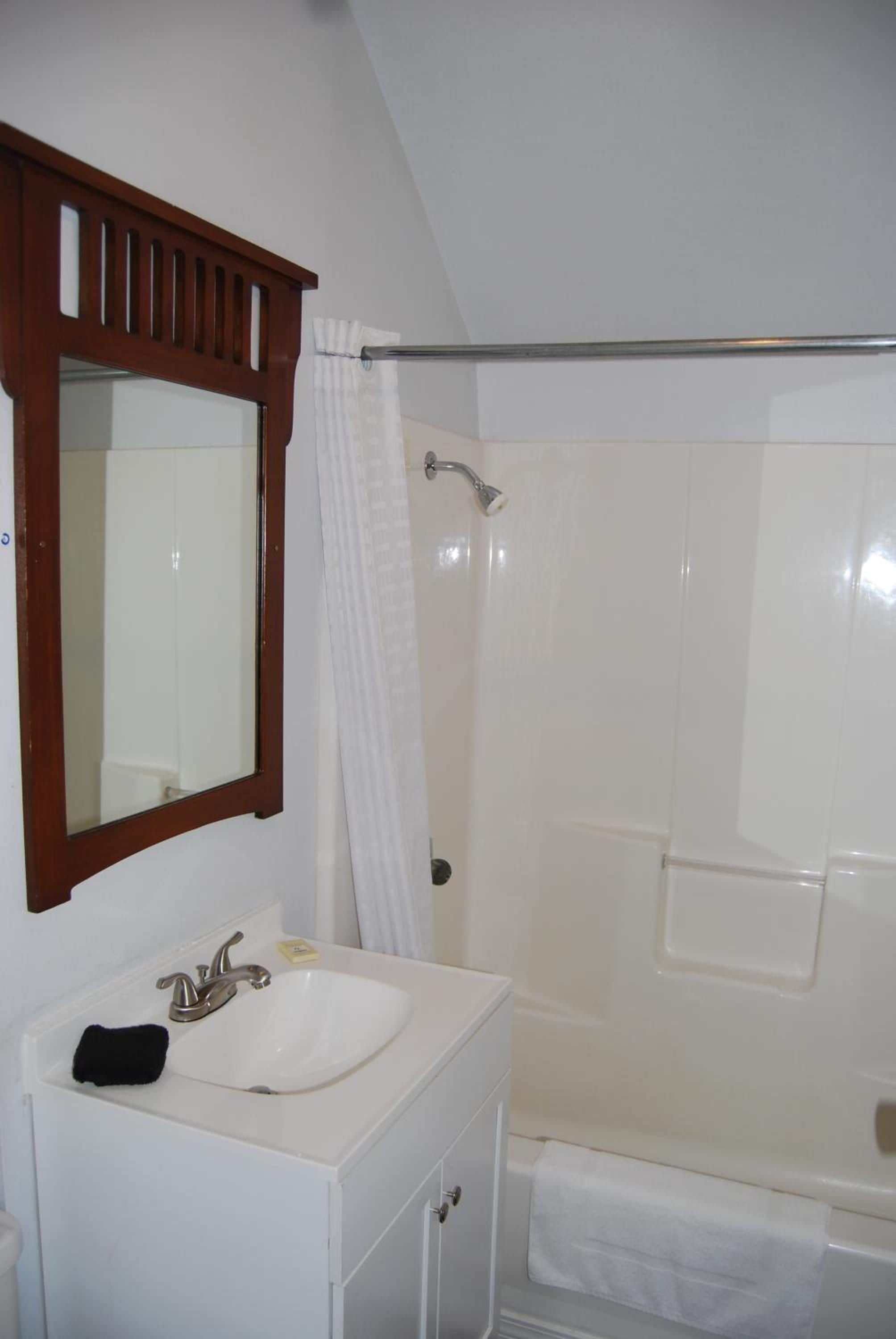 Een badkamer met een witte wastafel, een spiegel met houten lijst, een douche met witte douchegordijn en een witte badkuip.