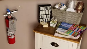 A small wooden desk with a fire extinguisher, a sign, a lamp, a potted plant, and a basket containing books and magazines. - Deep Water Inn (Chelan)