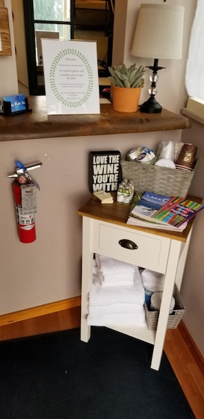 A small wooden desk with a fire extinguisher, a sign, a lamp, a potted plant, and a basket containing books and magazines. - Deep Water Inn (Chelan)