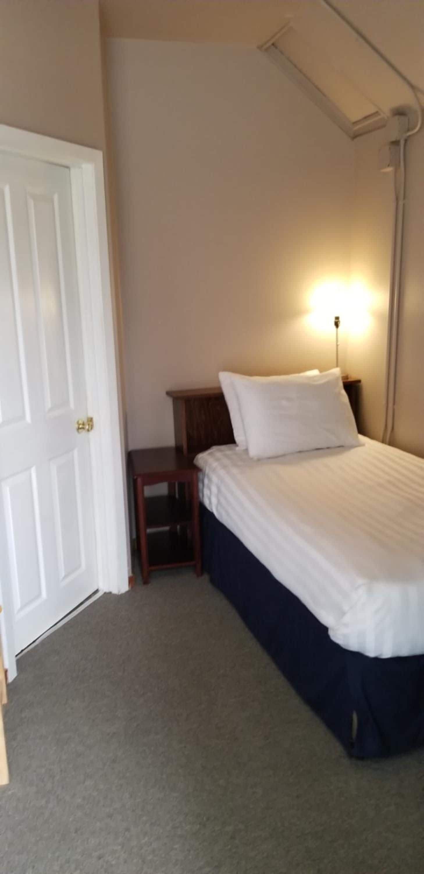 Une chambre à coucher avec un lit, une table de chevet, une lampe et une porte.