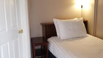A bedroom with a bed, a nightstand, a lamp, and a door.