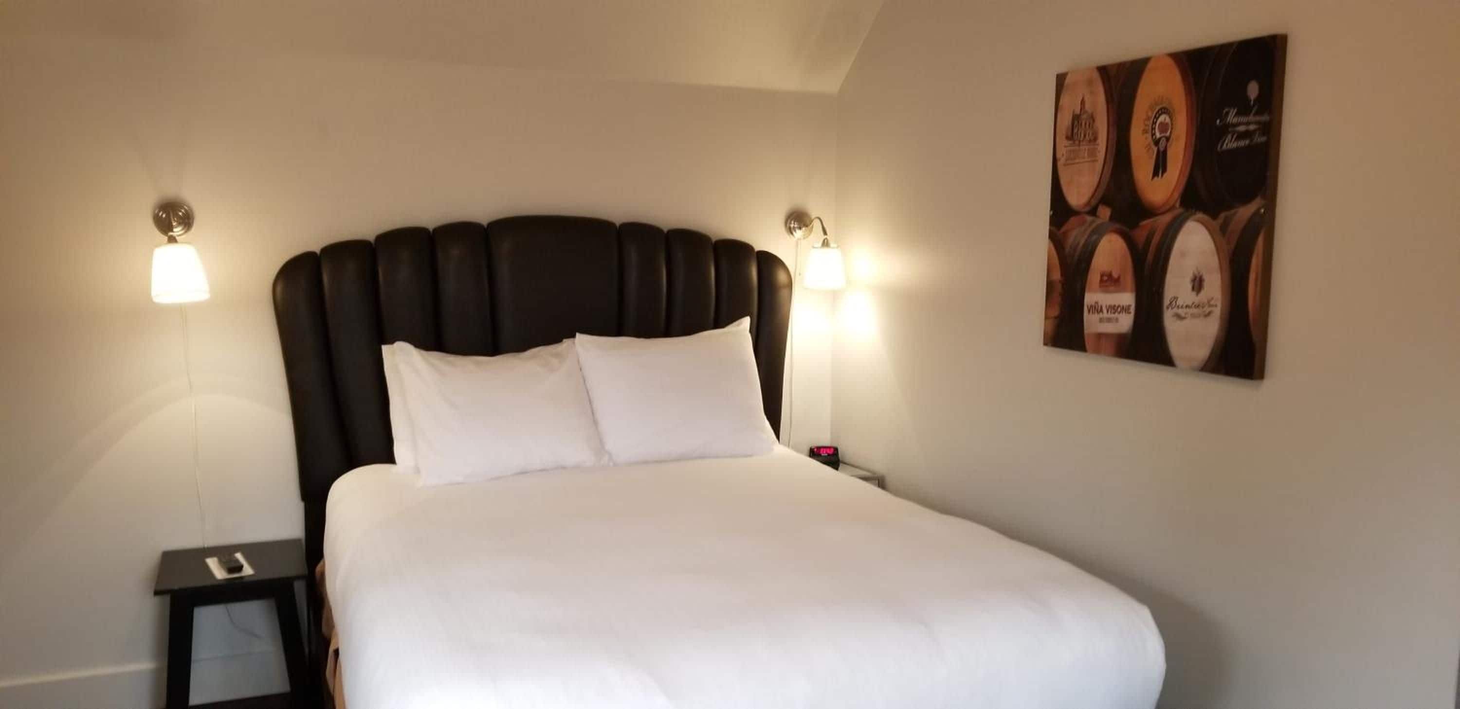 A hotel room with a large bed, two bedside lamps, a nightstand, and a wall-mounted poster.