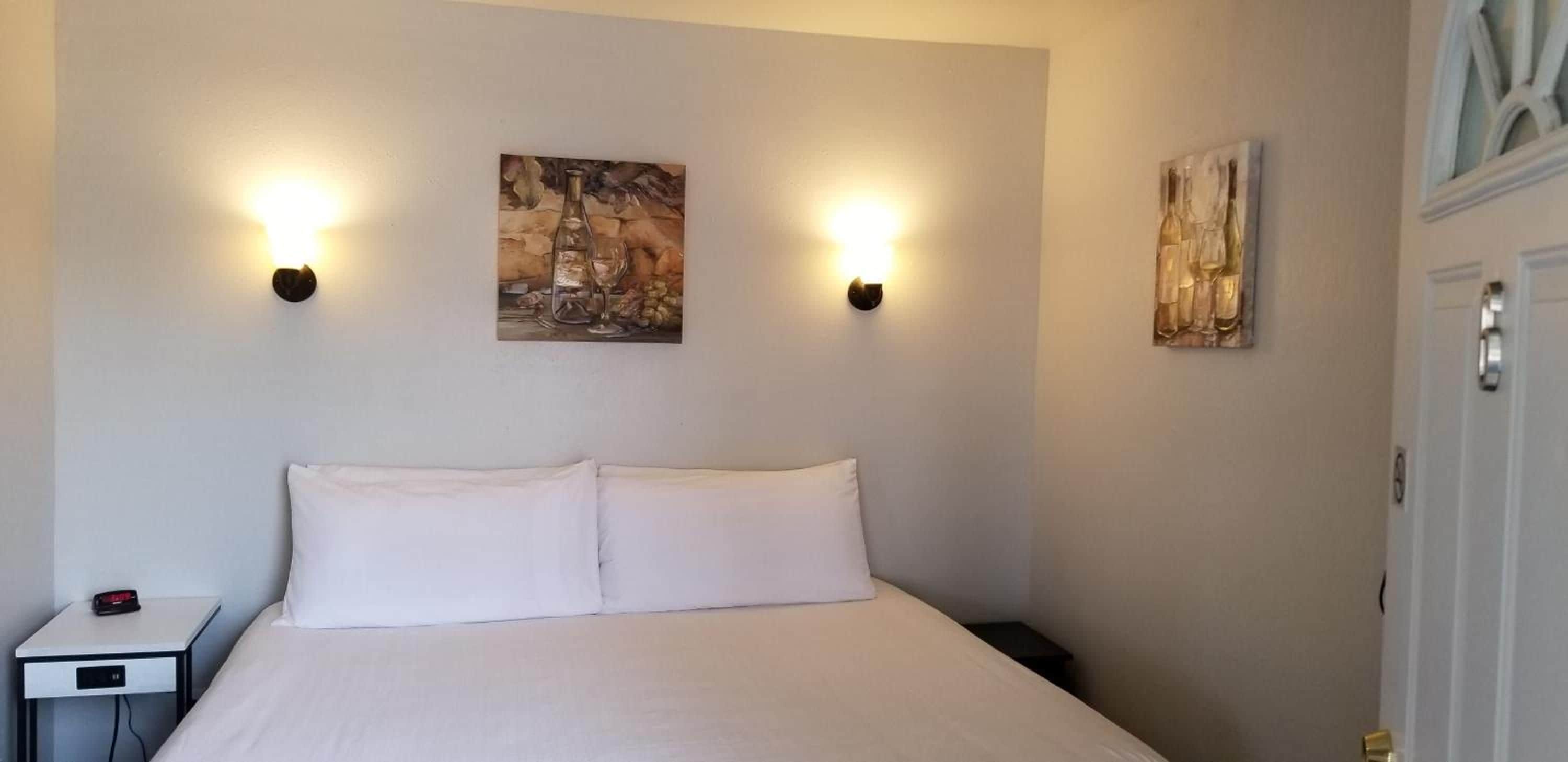 Ein Hotelzimmer mit einem Bett, zwei Wandleuchten und zwei Gemälden.