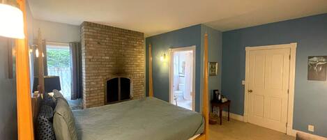 A bedroom with a bed, a brick fireplace, a door, and a small table with a coffee pot.