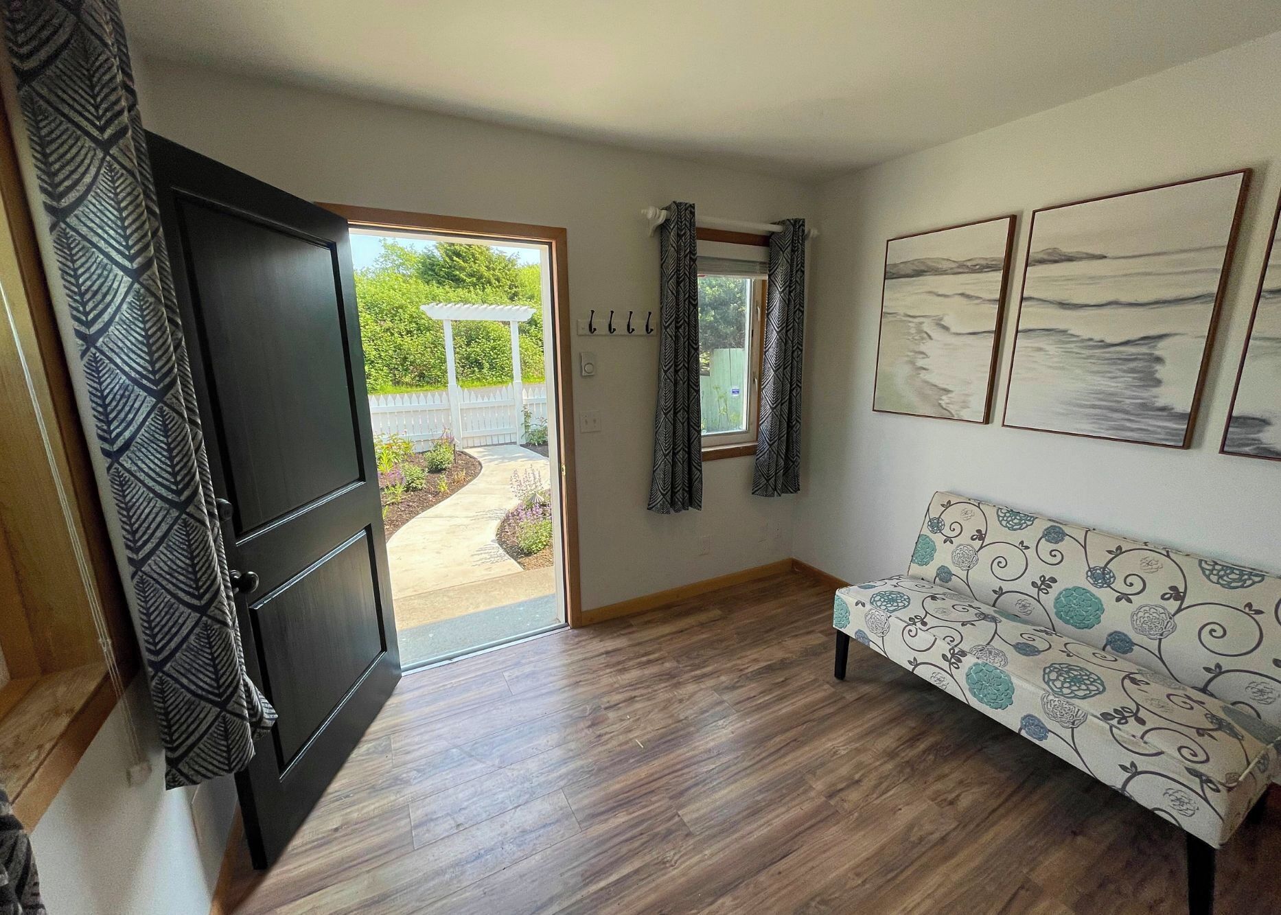 A room with a wooden floor, a sofa with a floral pattern, a door leading to an outdoor area, and three framed pictures on the wall.