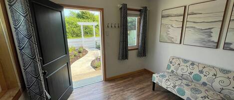 A room with a wooden floor, a sofa with a floral pattern, a door leading to an outdoor area, and three framed pictures on the wall.