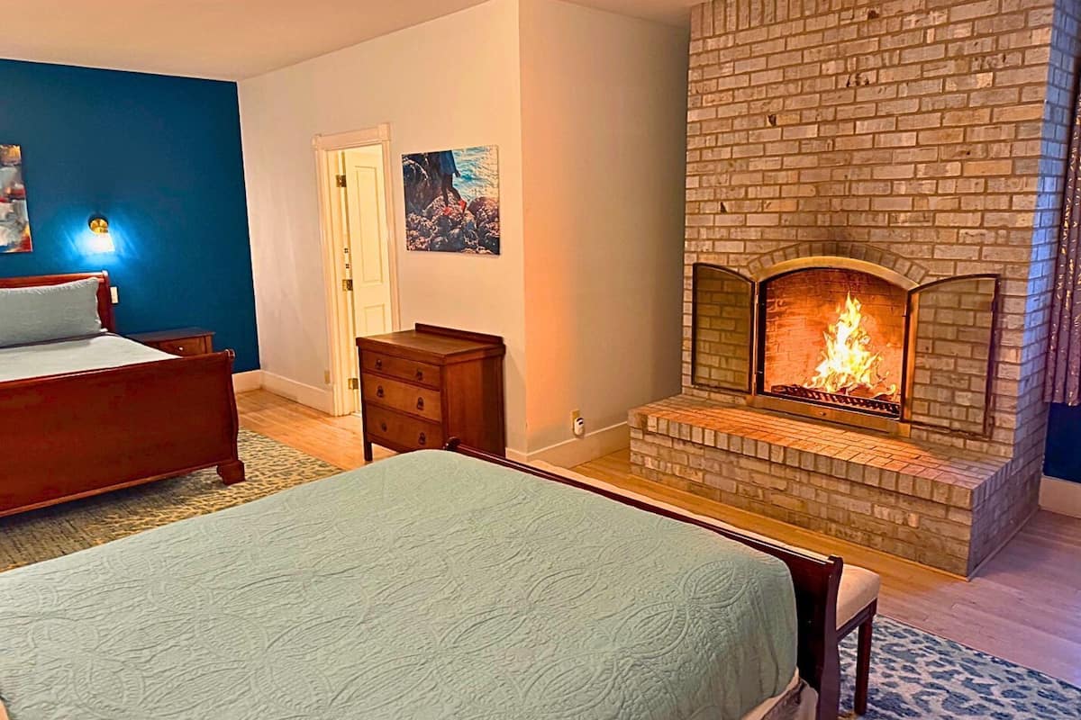 A bedroom with a brick fireplace, a bed, a dresser, and a door.