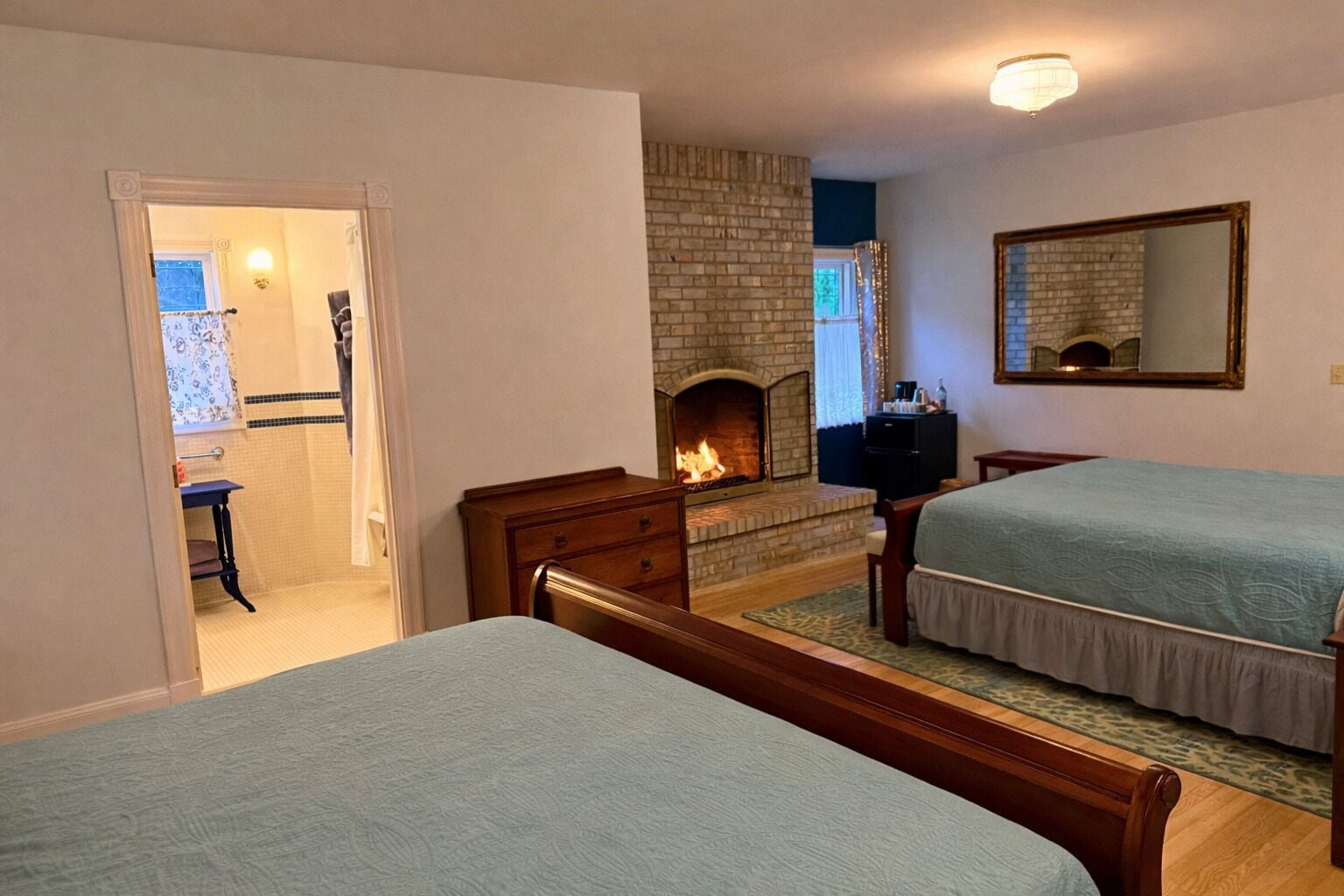 Een slaapkamer met twee bedden, een open haard, een spiegel en een deur naar een badkamer.