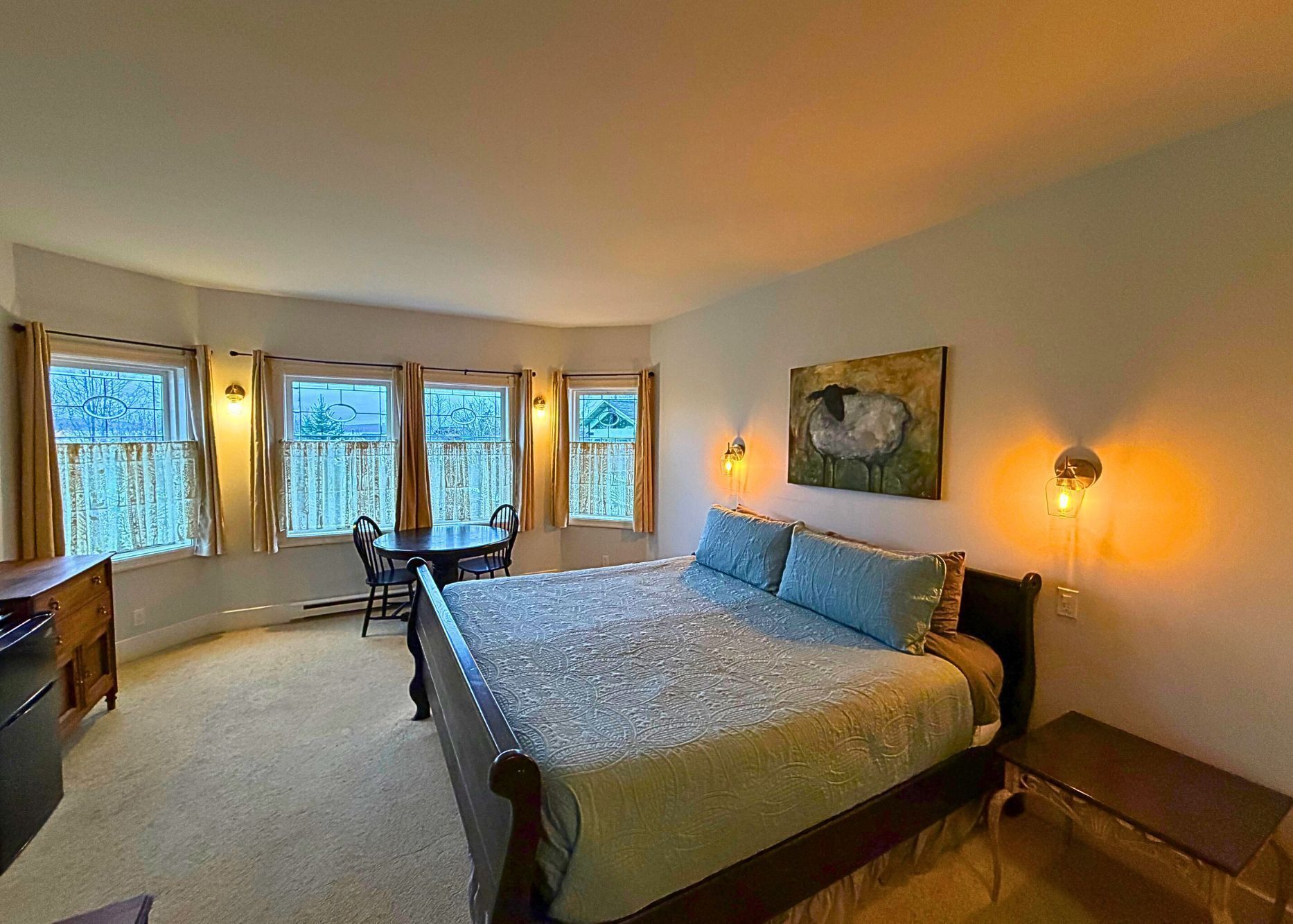 A bedroom with a large bed, a desk, a chair, and a window with curtains.