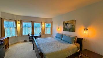 A bedroom with a large bed, a desk, a chair, and a window with curtains.