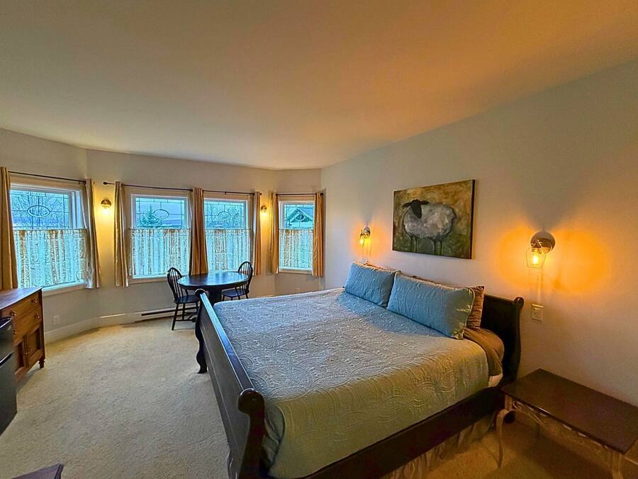 A bedroom with a large bed, a desk, a chair, and a window with curtains.