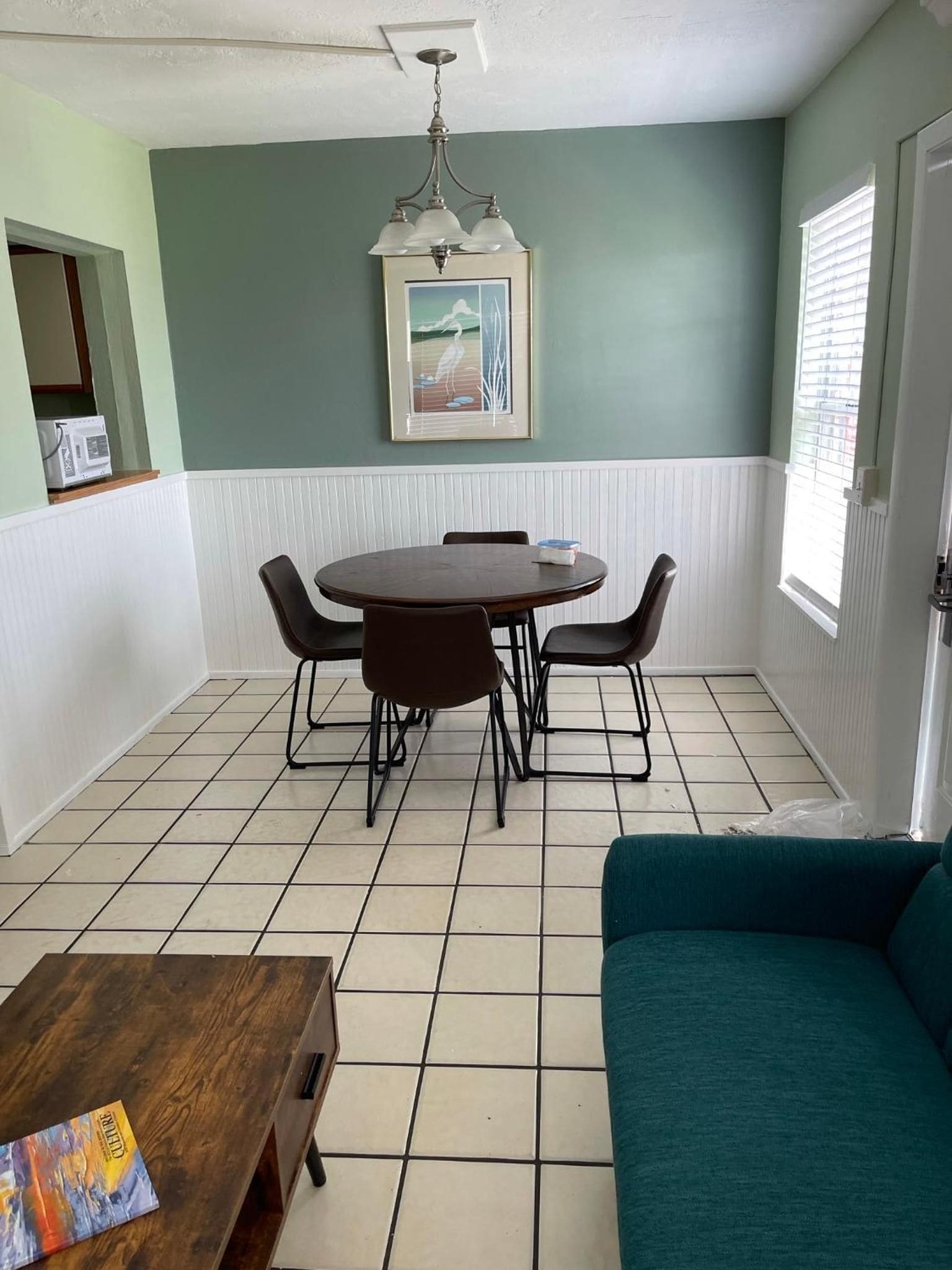 Un área de comedor con una mesa redonda y sillas, un sofá color turquesa y un cuadro en la pared.