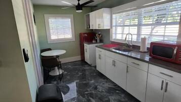 Una cocina con armarios blancos, un microondas rojo y un suelo de mármol negro.