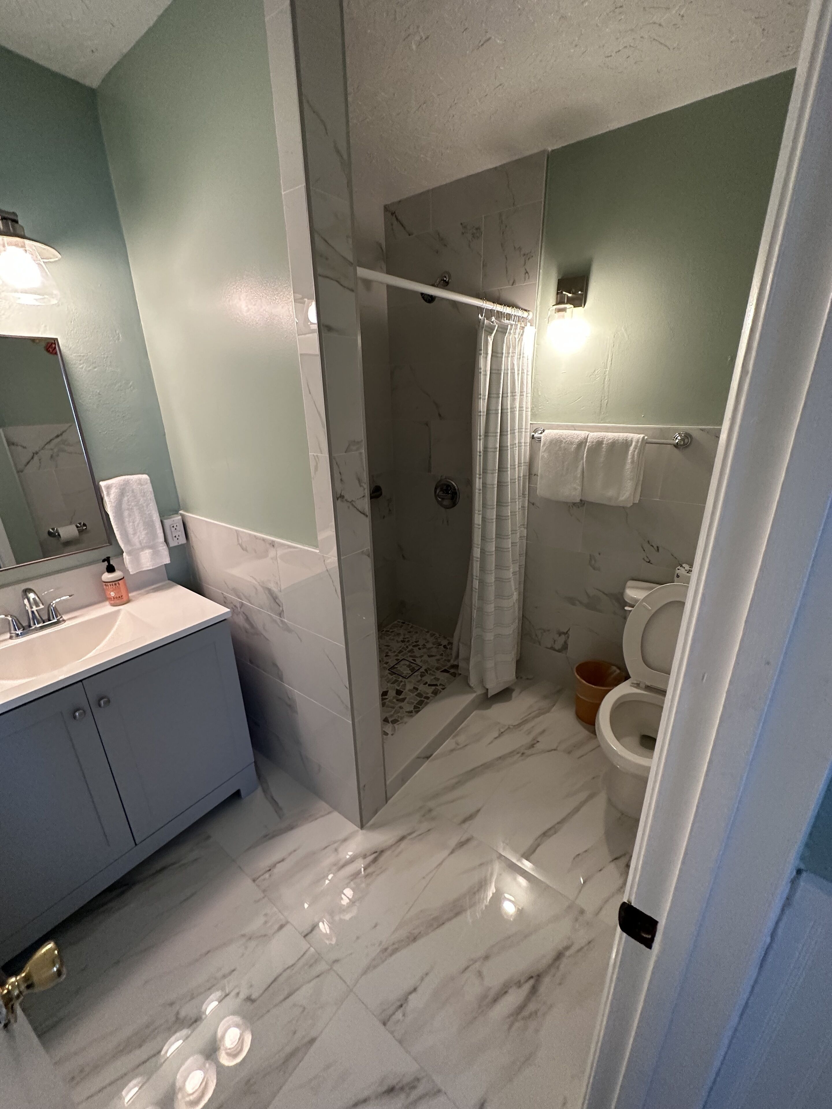 Une salle de bain avec un sol en marbre, une douche avec une porte en verre, des toilettes et un lavabo avec un miroir.