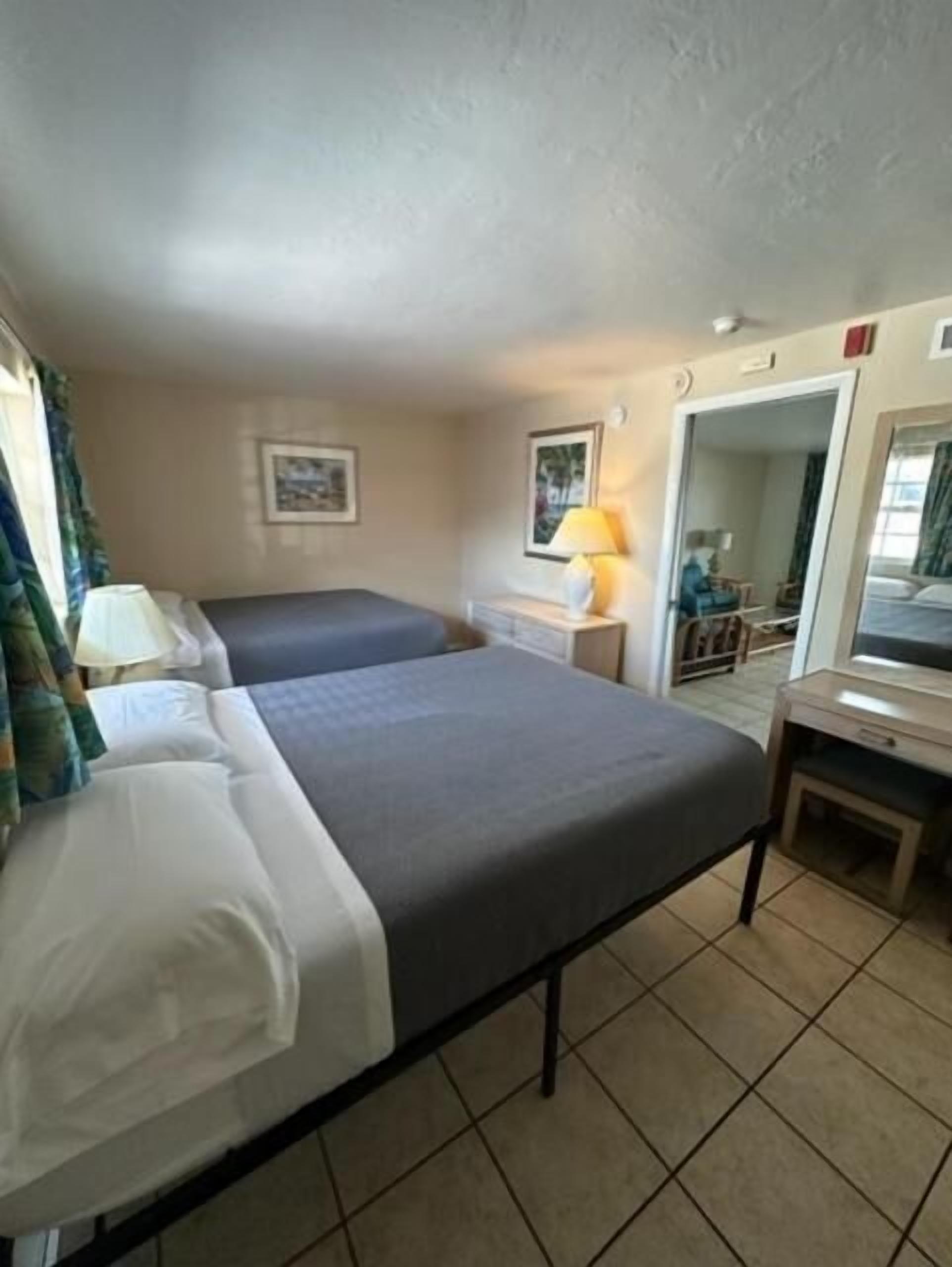 A hotel room with two beds, a desk, a chair, a lamp, and a mirror.
