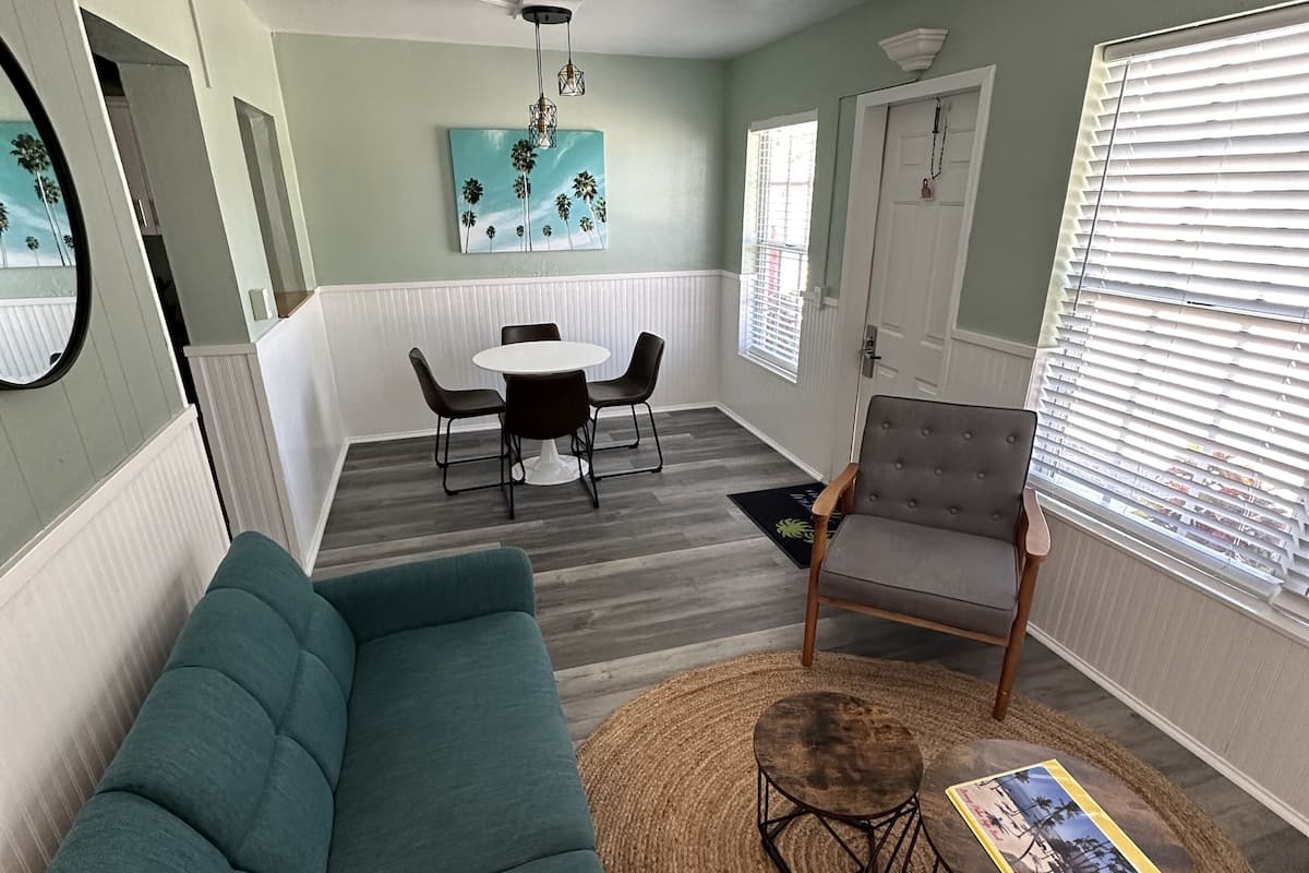 Un salon avec un canapé de couleur turquoise, une table à manger avec des chaises, un fauteuil gris et une table basse avec un magazine.