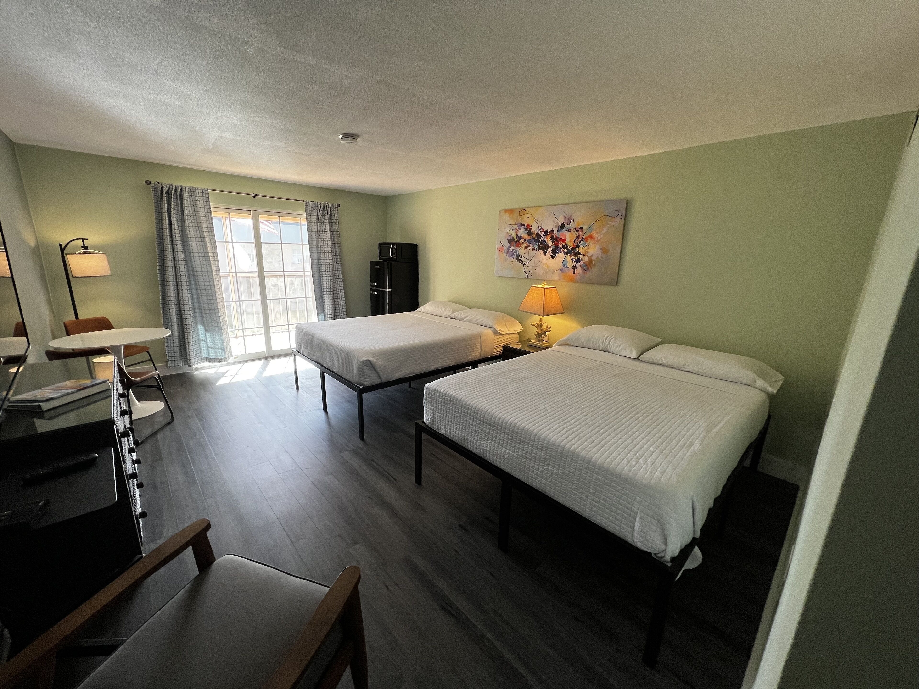 A hotel room with two beds, a desk, a chair, a lamp, and a painting on the wall.