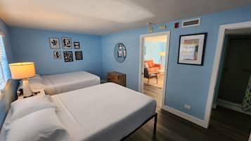 Une chambre avec deux lits, une table de chevet avec une lampe et une porte donnant sur une autre pièce.