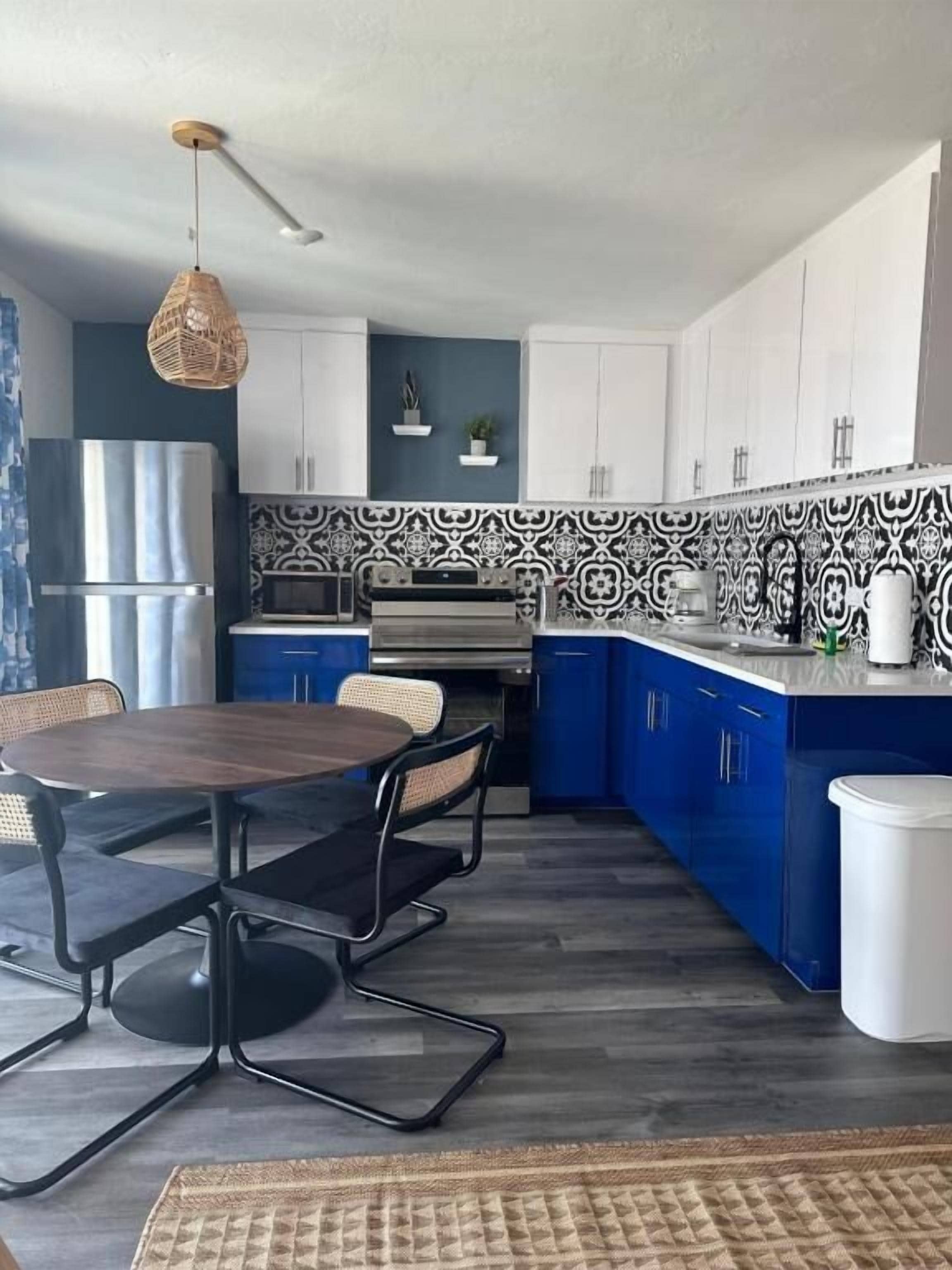 Uma cozinha compacta com área de refeições, design moderno com armários azuis, backsplash estampado e luminária pendente.
