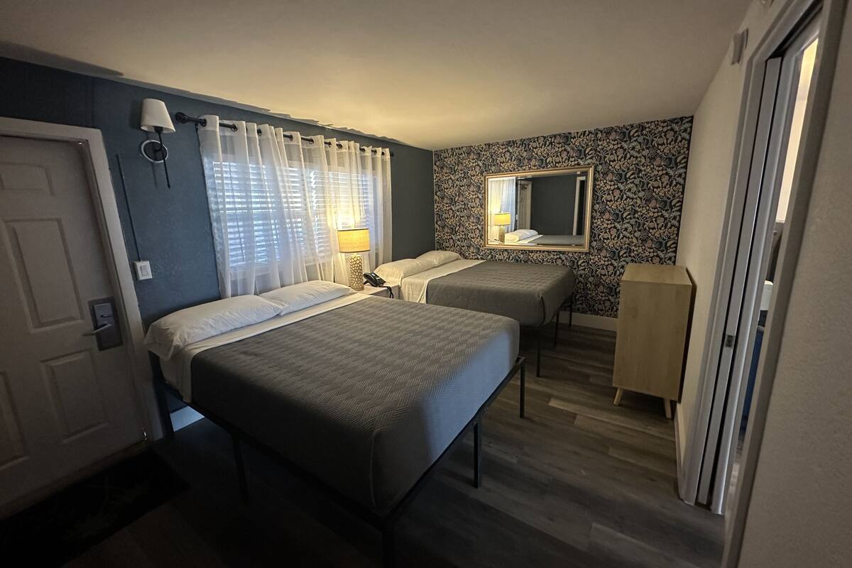 Une chambre d’hôtel avec deux lits, un bureau, un miroir et une armoire.