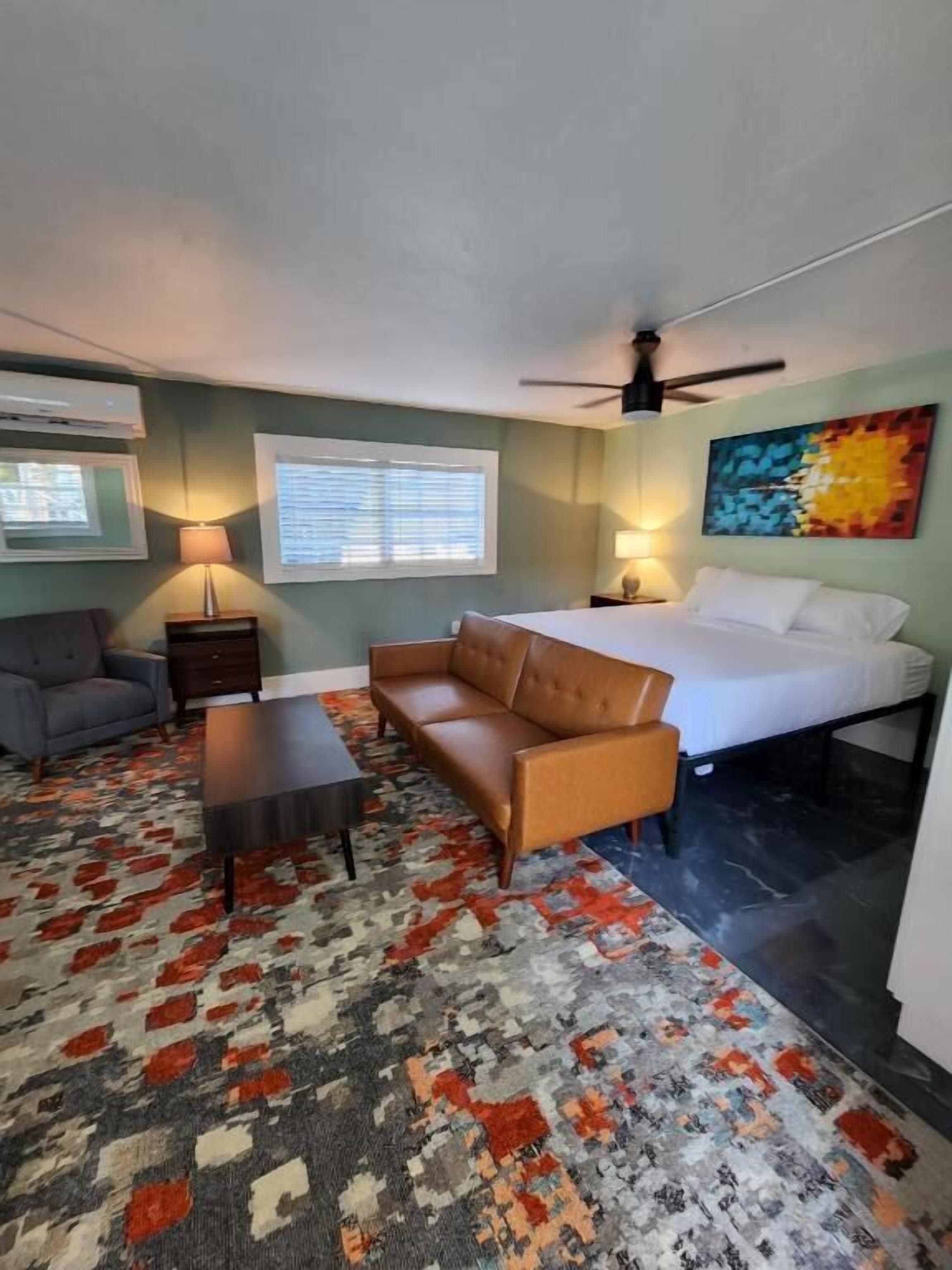 A hotel room with a bed, a sofa, a coffee table, a lamp, and a painting on the wall.