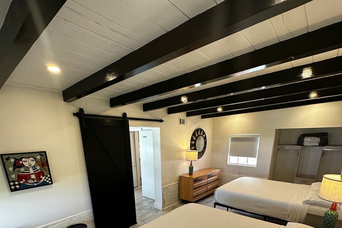 Une chambre d’hôtel avec un grand lit, une chaise en bois, une petite table et une commode.