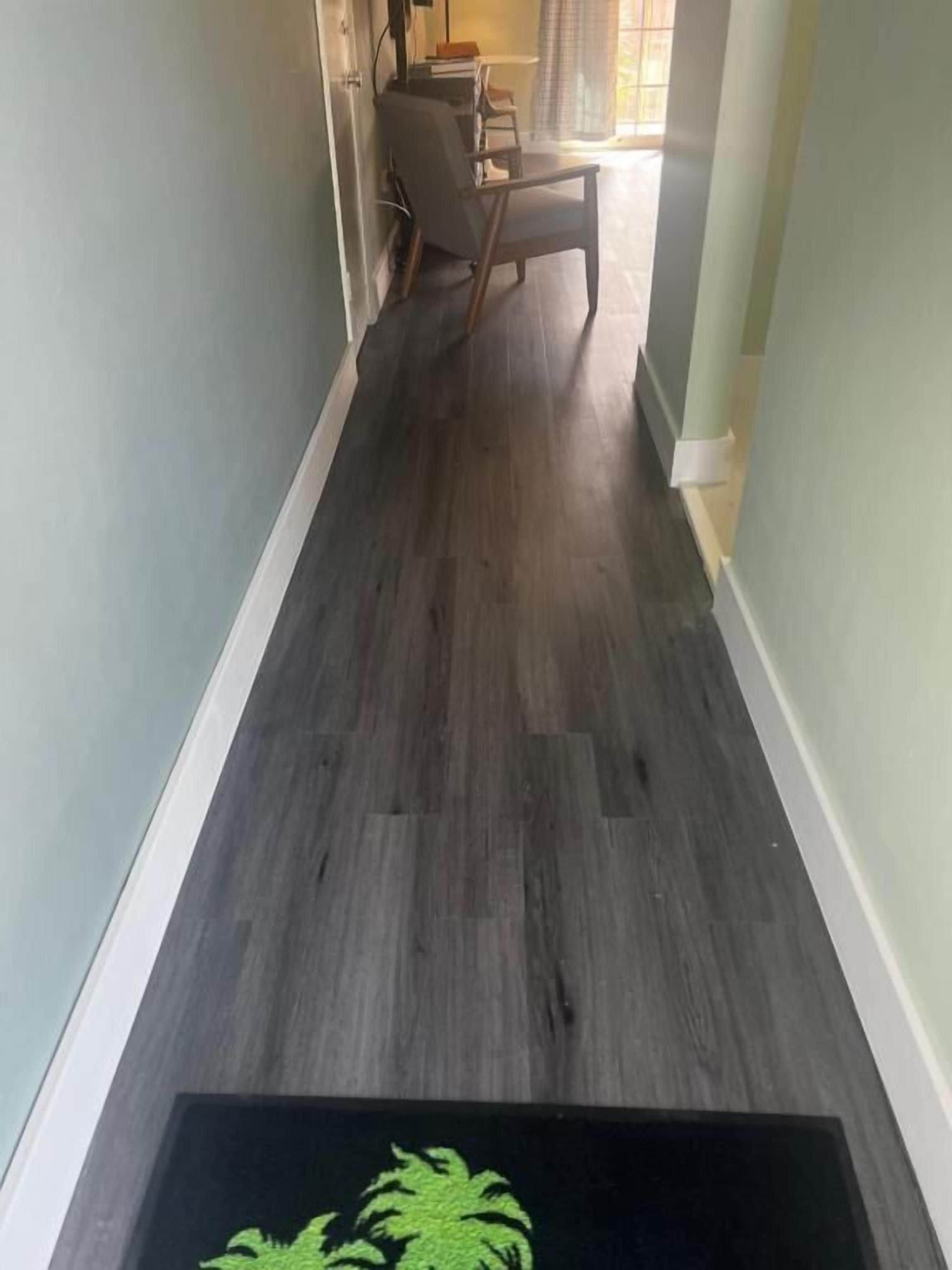 Een gang met een donker houten vloer, een stoel en een deur naar een andere kamer.