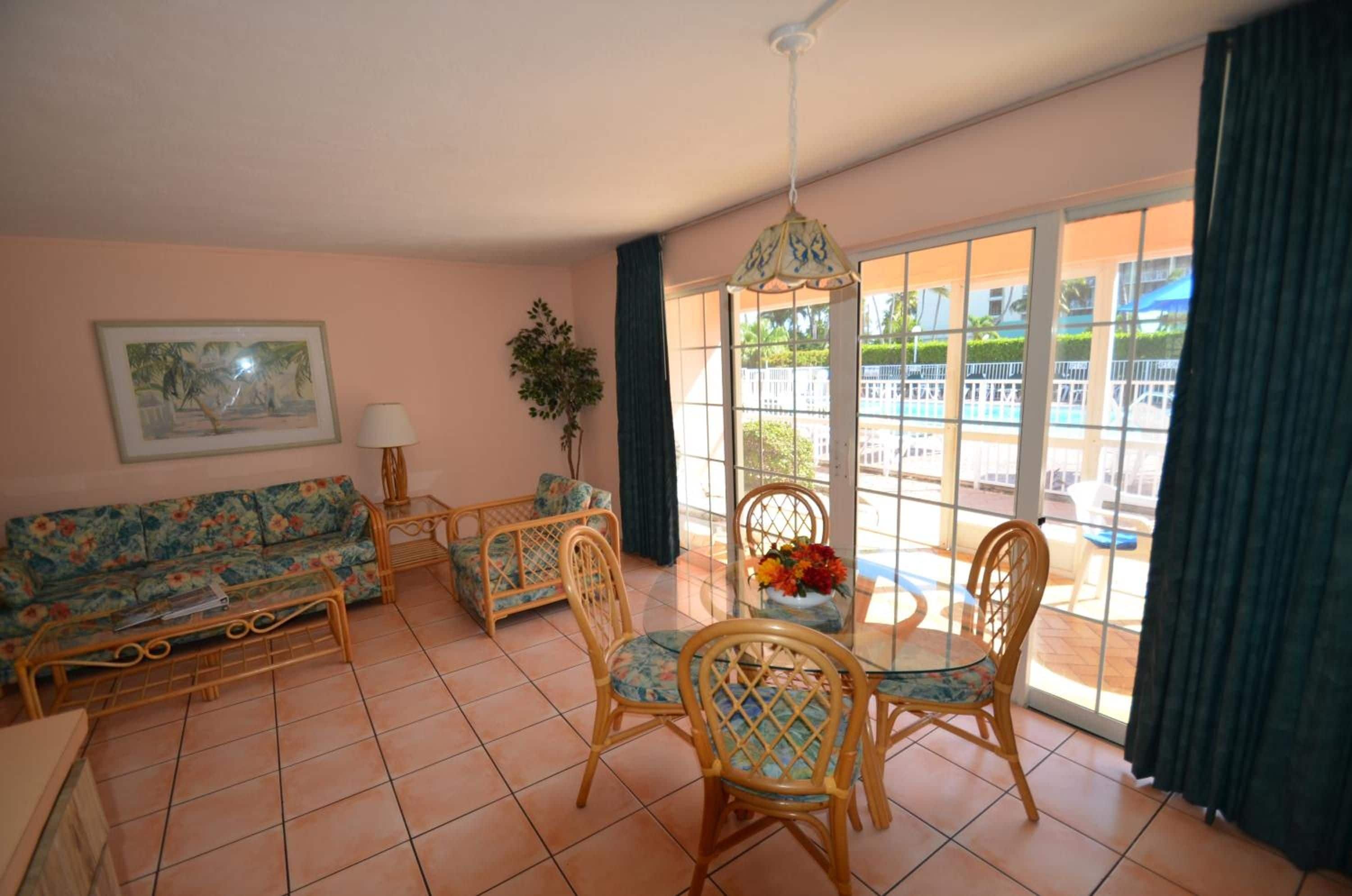 Un salon comprenant un canapé, des fauteuils, une table et donnant sur une piscine grâce à de grandes fenêtres.