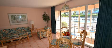 A living room with a sofa, chairs, a table, and a view of a pool through large windows.
