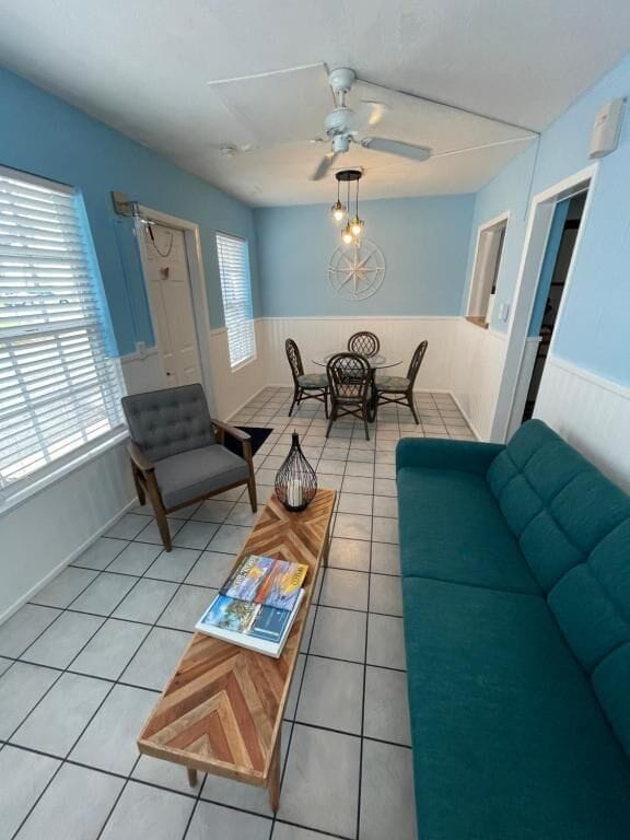 A room with a teal sofa, a wooden coffee table with magazines, a dining table with chairs, and a ceiling fan.
